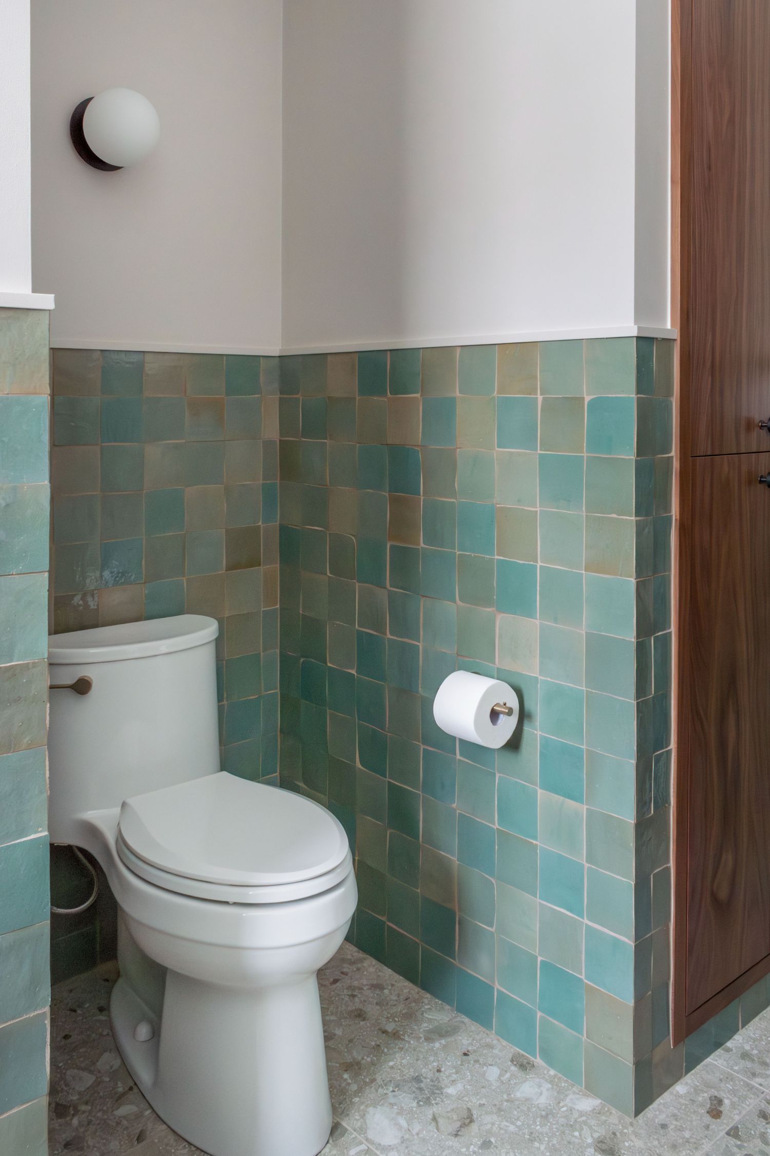 Kohler Adiar toilet with Lili Agave Green Zellige Tile on wall. round wall sconce in bathroom