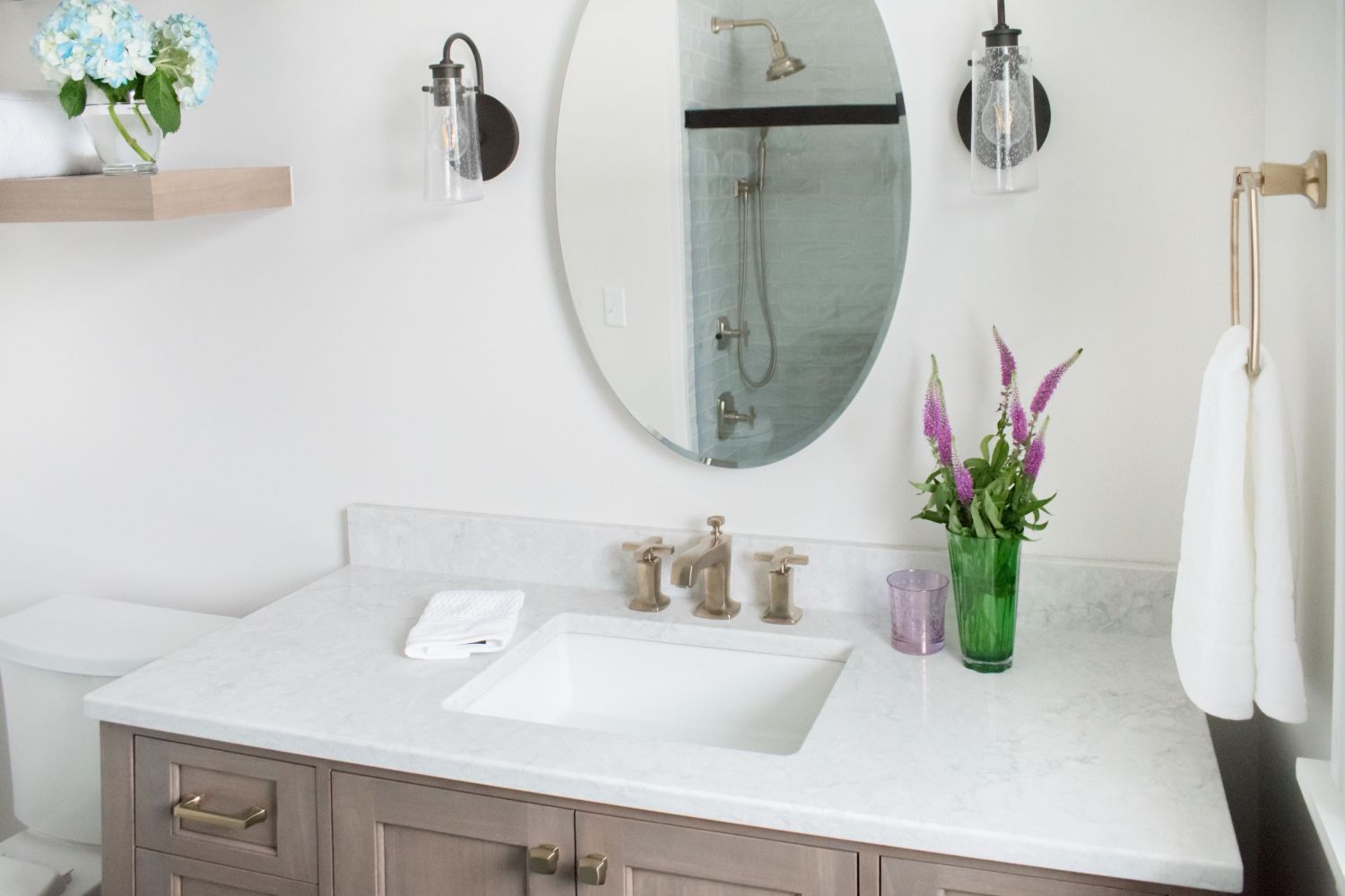 Bathroom Oval mirror with wall sconces Kohler Margaux faucet floating shelf